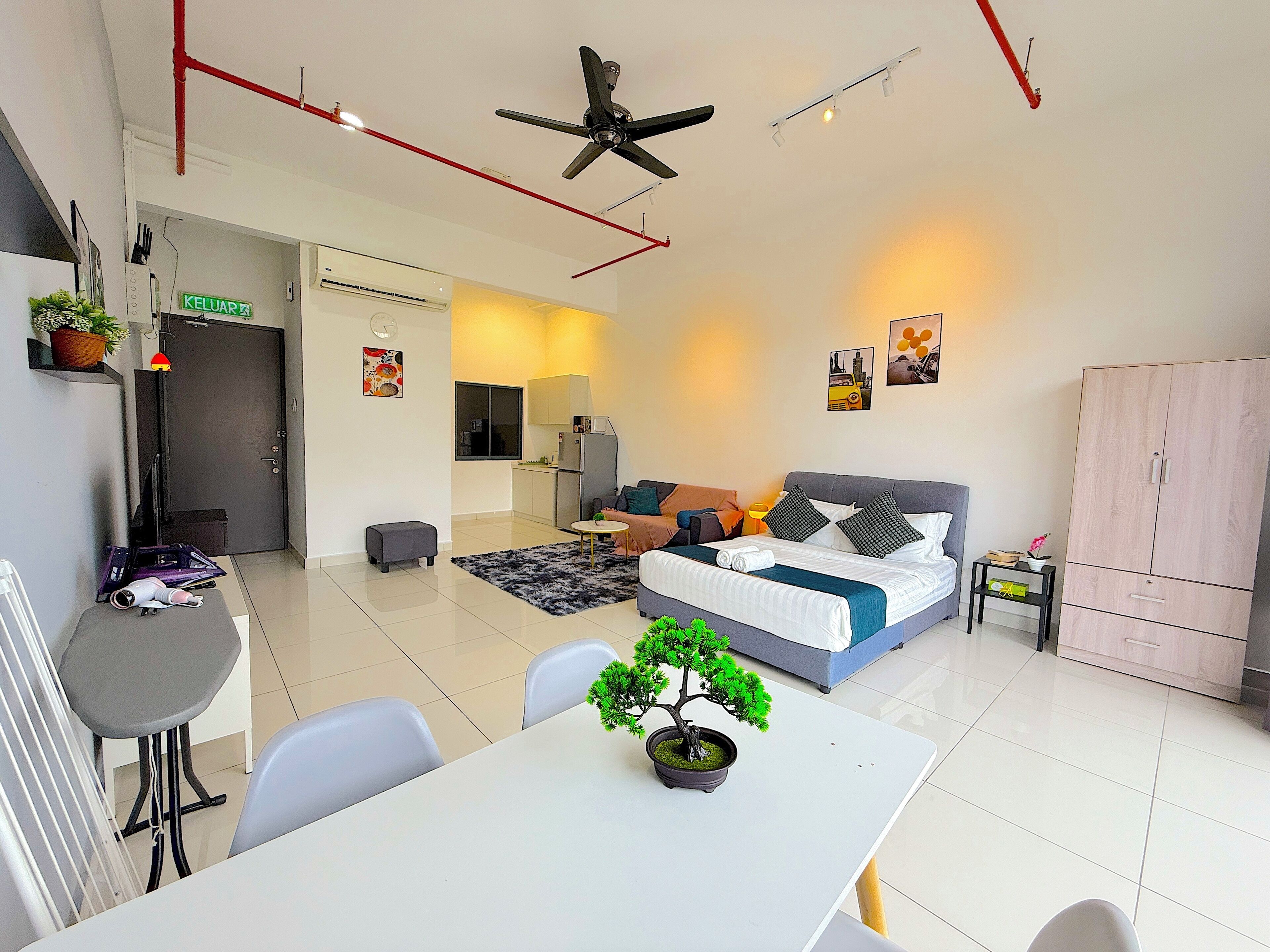 A modern apartment with a dining area, kitchenette, and a bedroom with a bed and seating area.