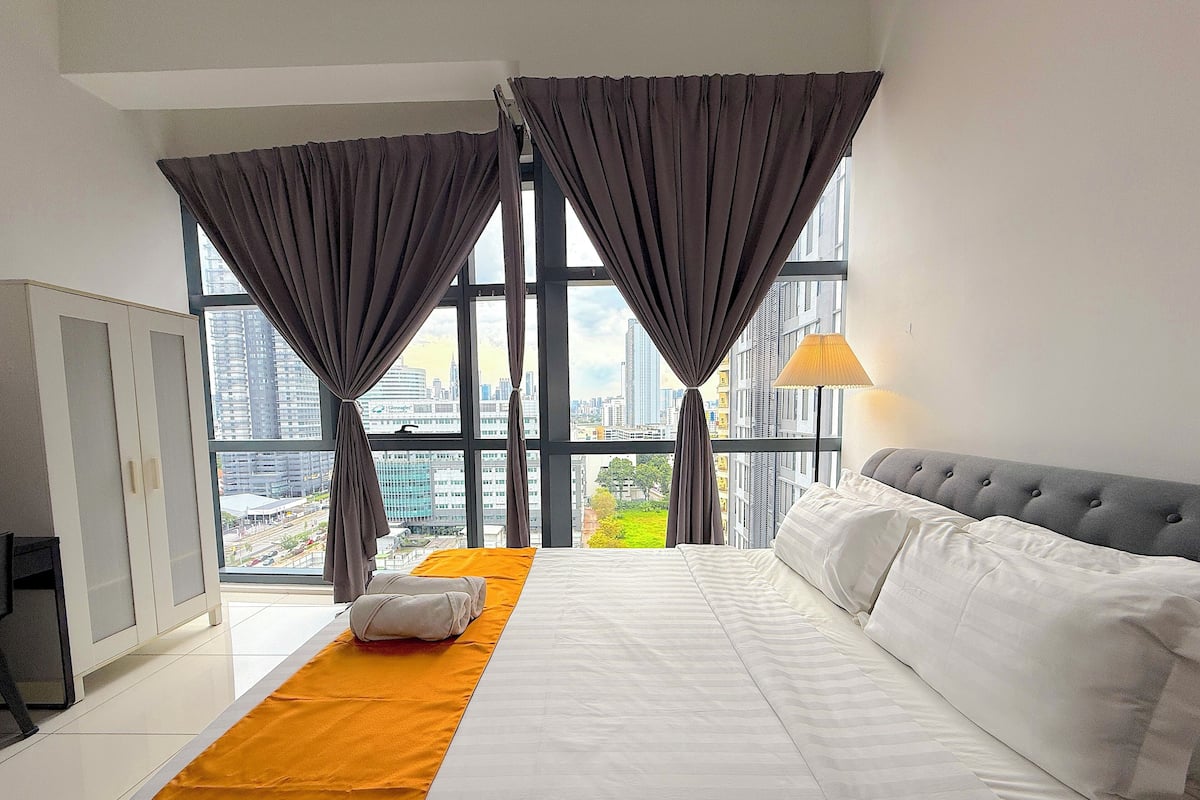 A hotel room with a large bed, a view of the cityscape, and a wardrobe.
