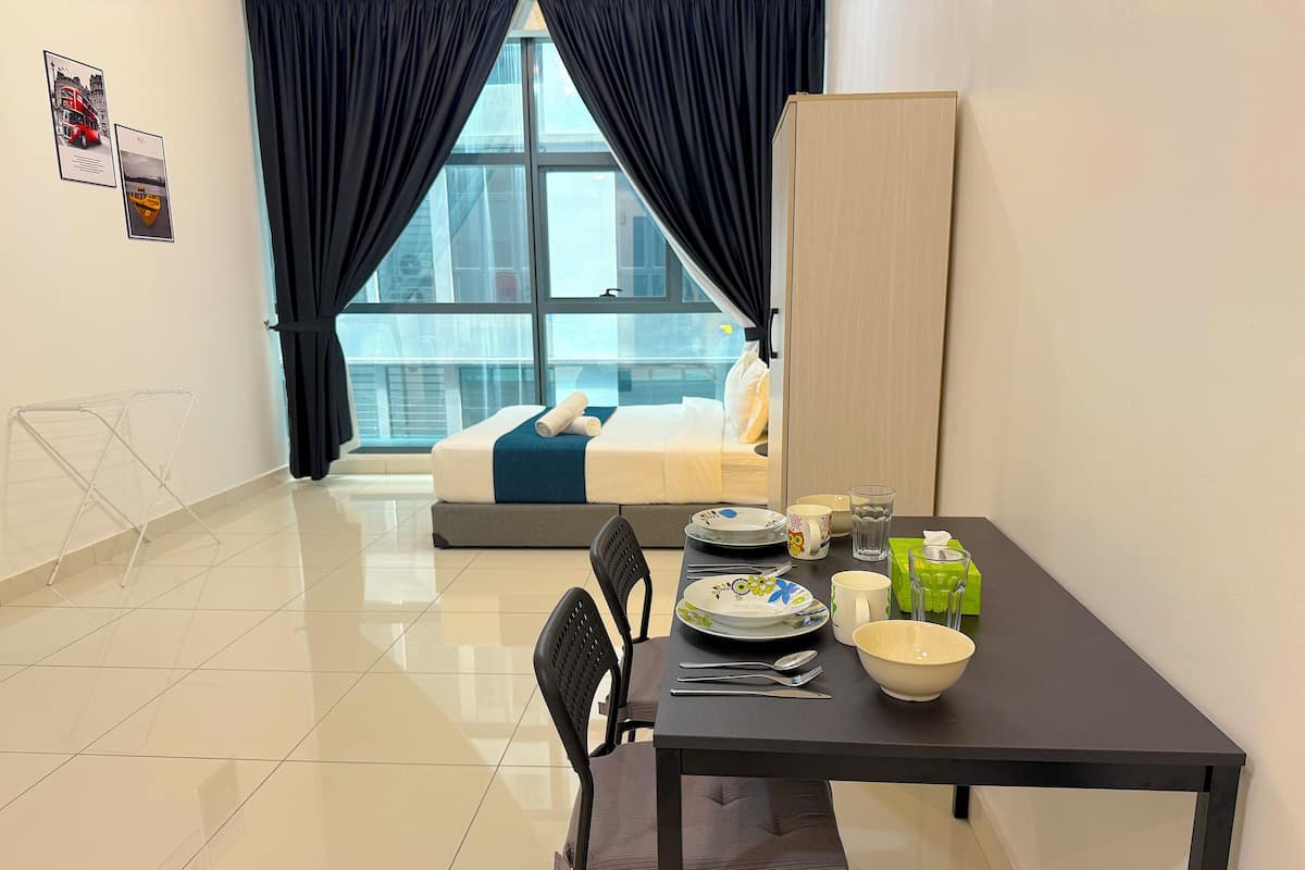 A hotel room with a bed, a dining table with chairs, a window with curtains, and a view of the city.