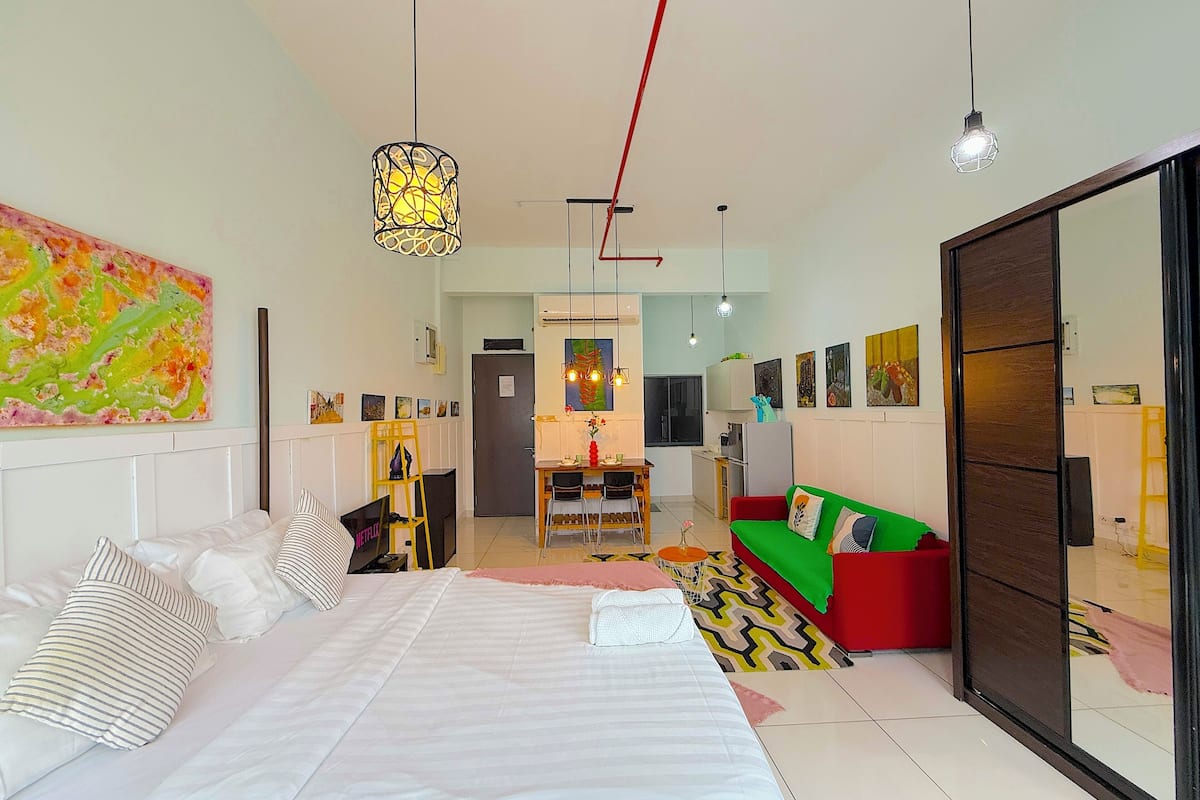 A modern bedroom with a large bed, a dining area, and a living space with a sofa and a TV.