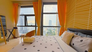 A hotel room with a large bed, a chair, a small table, and a view of the cityscape through large windows. - 3 Towers Jalan Ampang By Serenity Homes (Kuala Lumpur)