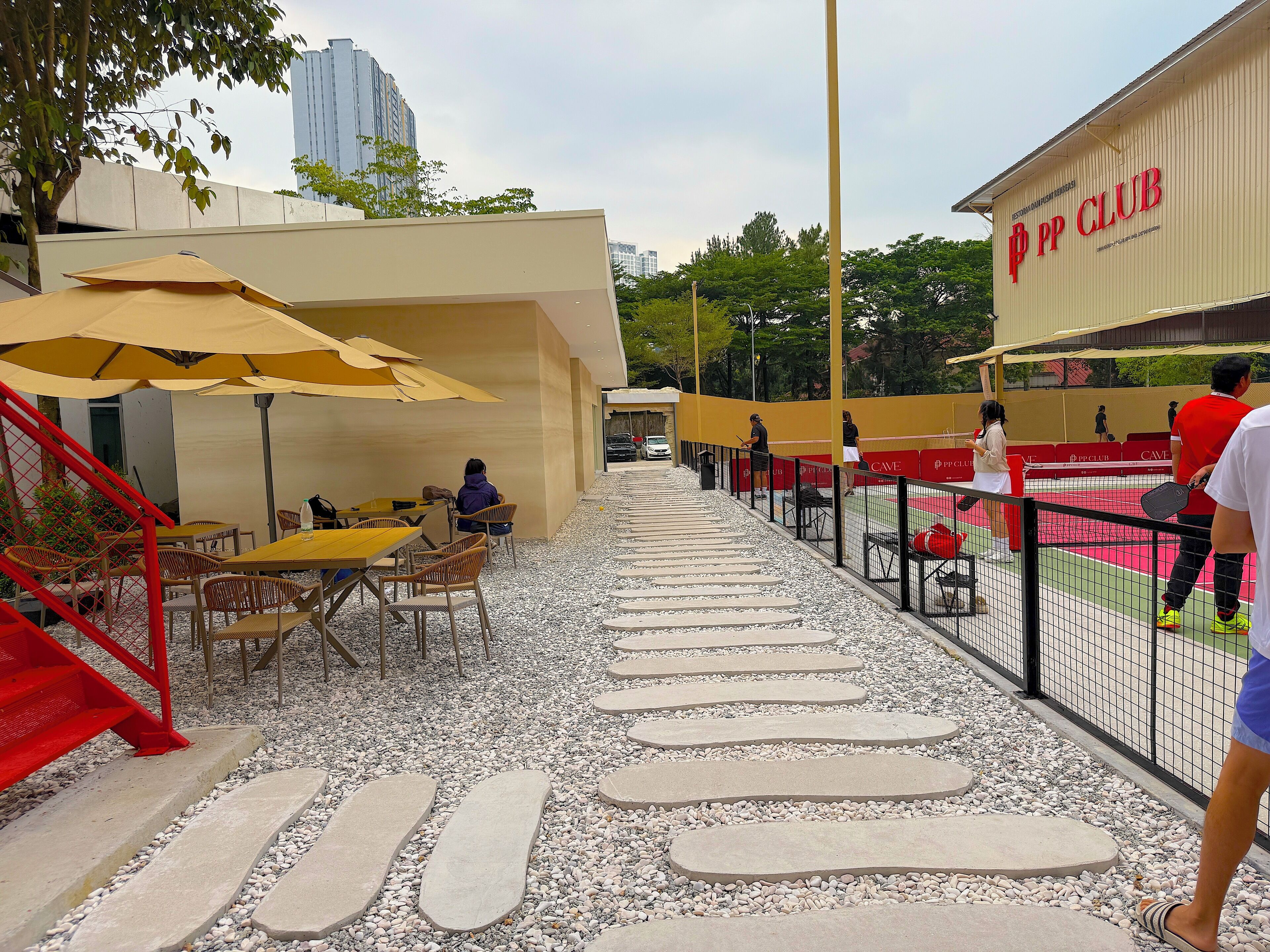 An outdoor seating area with tables and chairs, a tennis court, and a building labeled "PP CLUB".