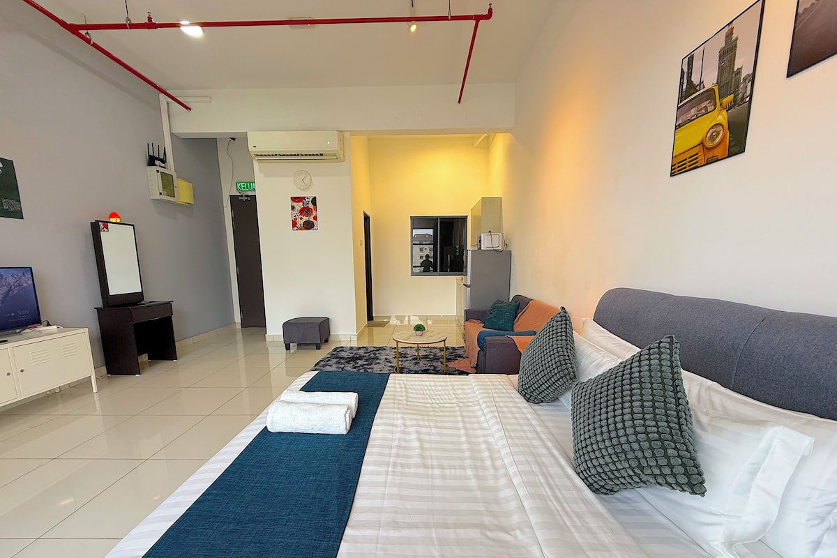 A hotel room with a large bed, a desk with a computer, a small table with a plant, and a sofa.