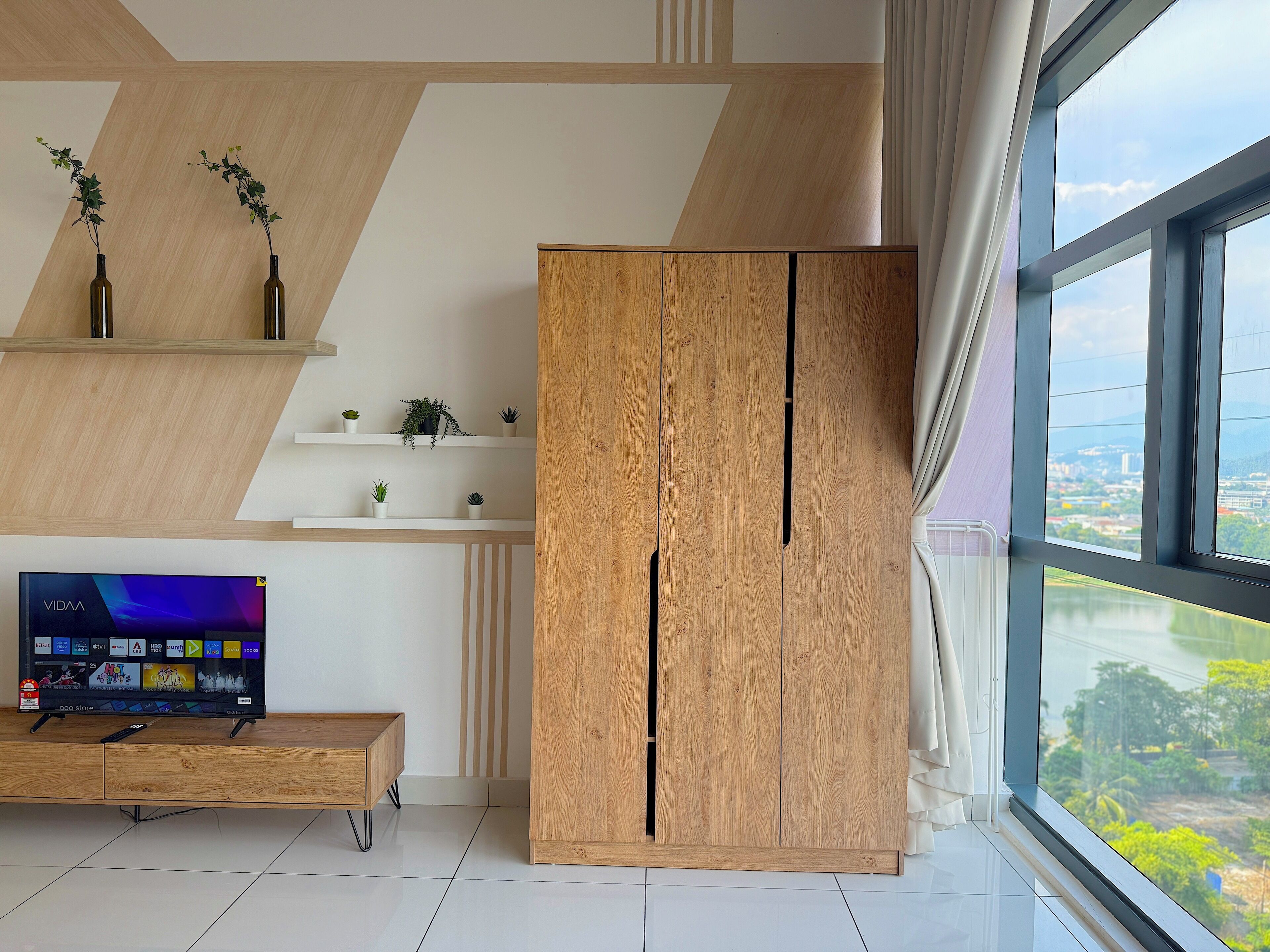 A modern living room with a wooden cabinet, a TV on a wooden stand, and a view through large windows.