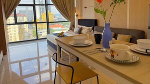A modern hotel room with a large window, a bed with a view, a dining area with a table set for two, and a vase with flowers. - 3 Towers Jalan Ampang By Serenity Homes (Kuala Lumpur)
