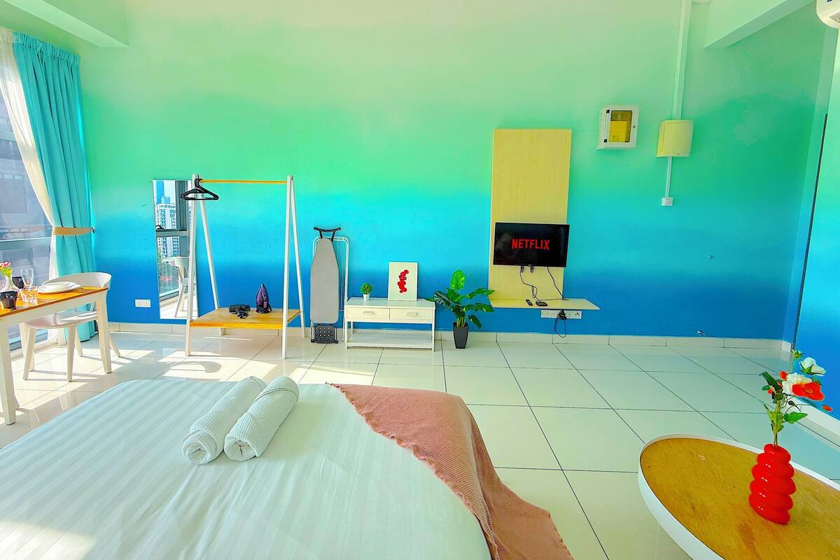 A hotel room with a bed, a desk, a chair, a TV, and a window with curtains.