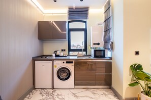 A compact kitchen with a washing machine, a coffee maker, and a microwave. - The Platine Plus Suite (Istanbul)