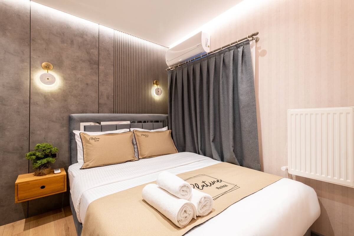 A neatly made bed with a towel, a bedside plant, and a nightstand with a lamp.