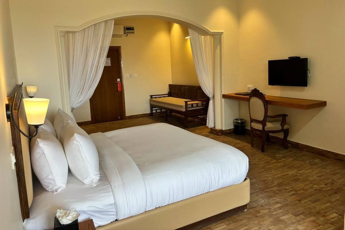 A hotel room with a large bed, a desk, a chair, a TV, and a lamp.