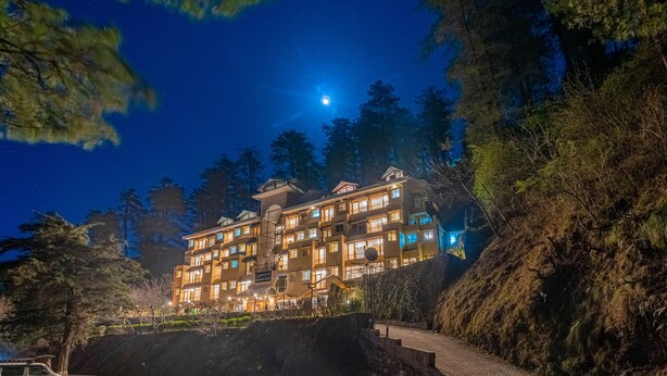 Hotel de varios pisos con una fachada bien iluminada, rodeado de árboles y un cielo nocturno despejado.