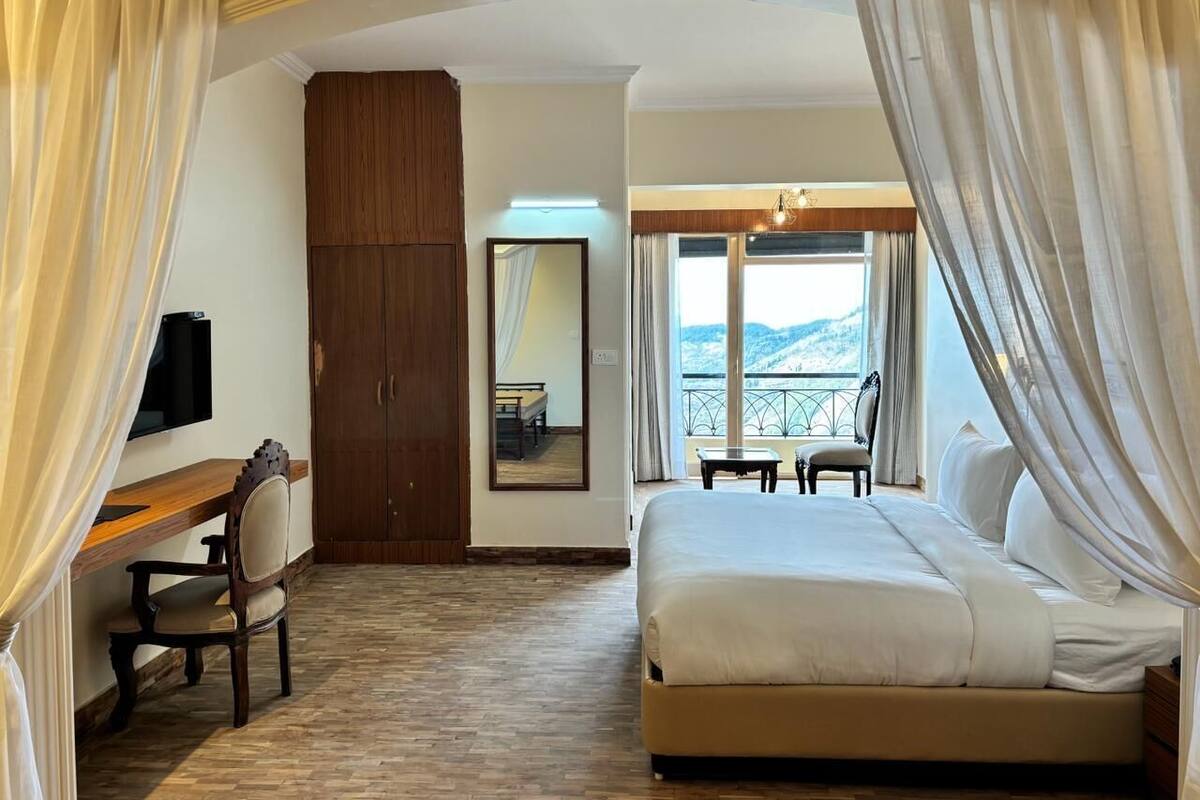 A hotel room with a bed, a desk, a chair, a wardrobe, a TV, and a balcony with a view.