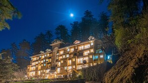 Un hotel de varios pisos con una fachada bien iluminada, rodeado de árboles y un cielo nocturno despejado.