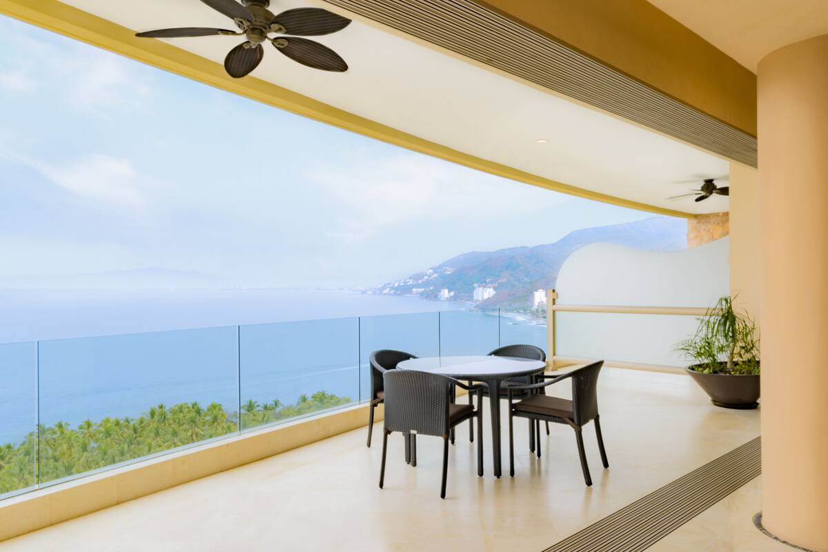 Un balcon avec une table et des chaises, offrant une vue sur la côte, avec des montagnes et la mer.