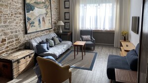 A living room with a stone wall, a sofa, a chair, a wooden chest, and a large painting. - Villa Classée Face Mer, Petit Jardin , Veranda et Terrasse Ensoleillée, 120 m2, (La Baule-Escoublac)
