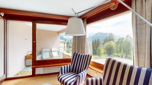 Una stanza con un'ampia finestra, una ventola a soffitto, una poltrona a righe e vista su un paesaggio montano.