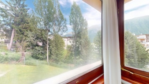 Vista dalla finestra su una zona montuosa con alberi e edifici.