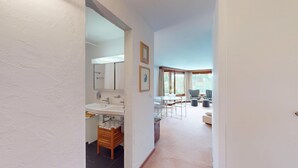 Un corridoio che conduce a un bagno con lavandino e specchio, una zona pranzo con tavolo e sedie, e vista sull'esterno.