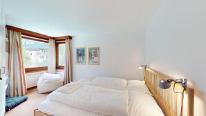 Una camera da letto con un letto, cuscini, un comodino con una lampada, una finestra con tende e due quadri appesi al muro.