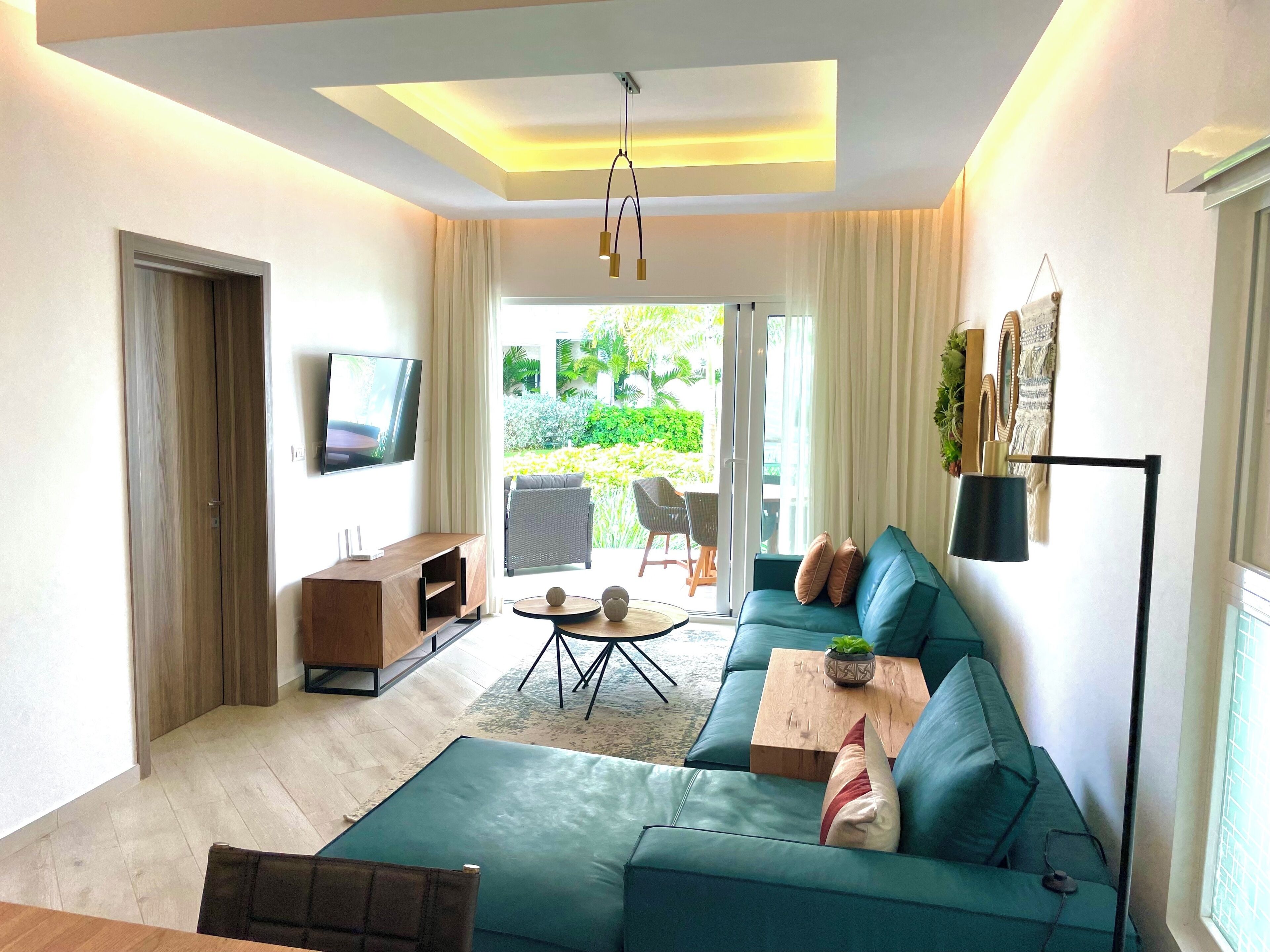 A modern living room with a teal sofa, a wooden coffee table, and a flat-screen TV mounted on the wall.