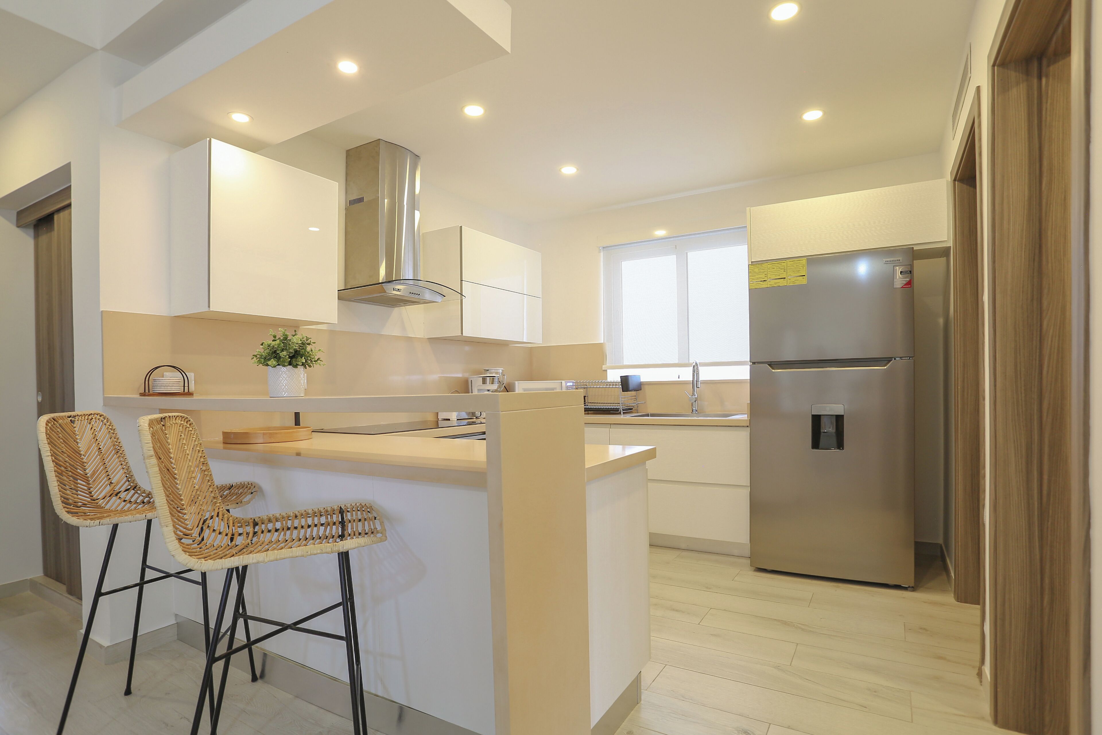 A modern kitchen with a central island, stainless steel appliances, and wicker bar stools.