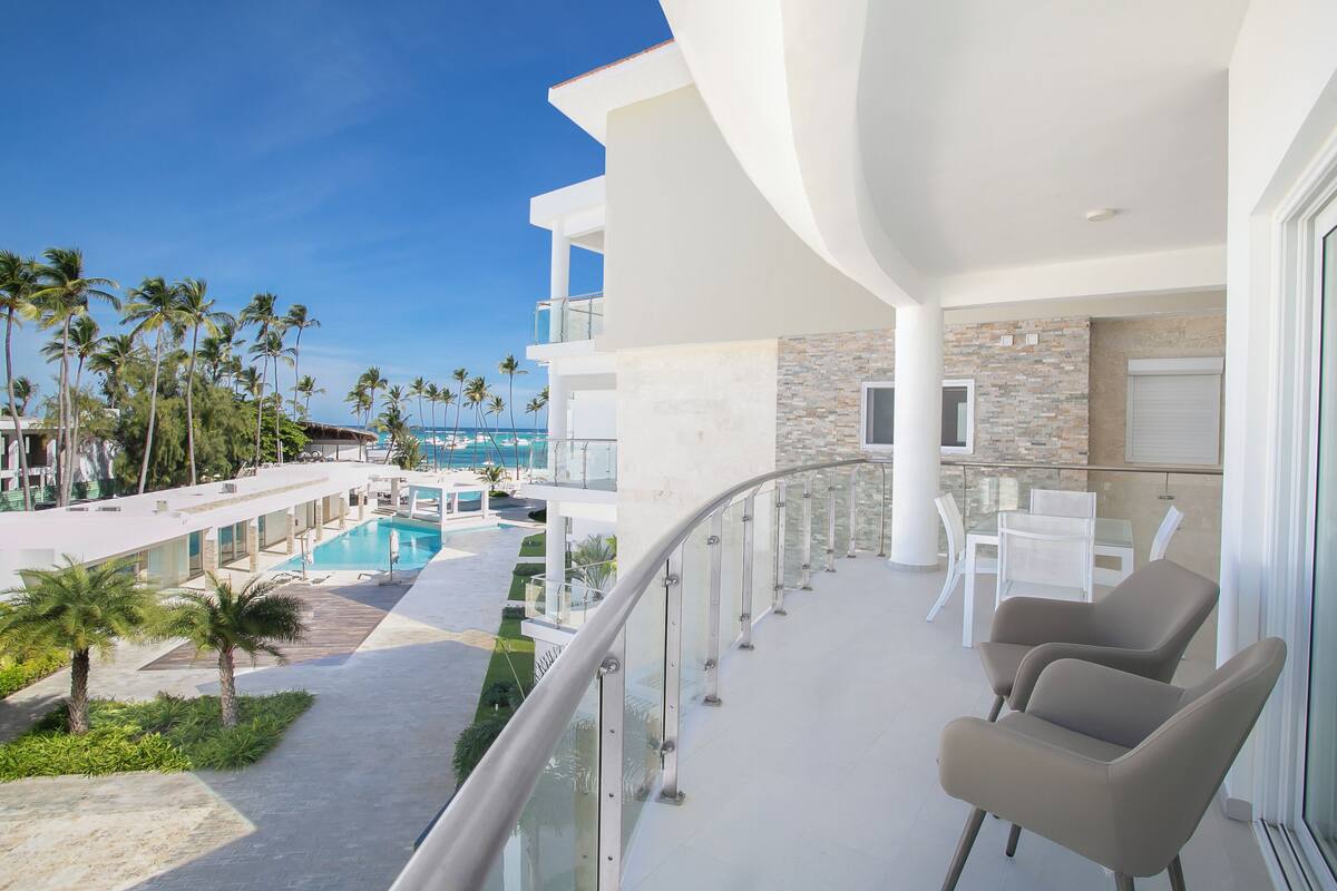 Un balcon donnant sur la piscine, des meubles d’extérieur blancs et un ciel d’un bleu limpide.