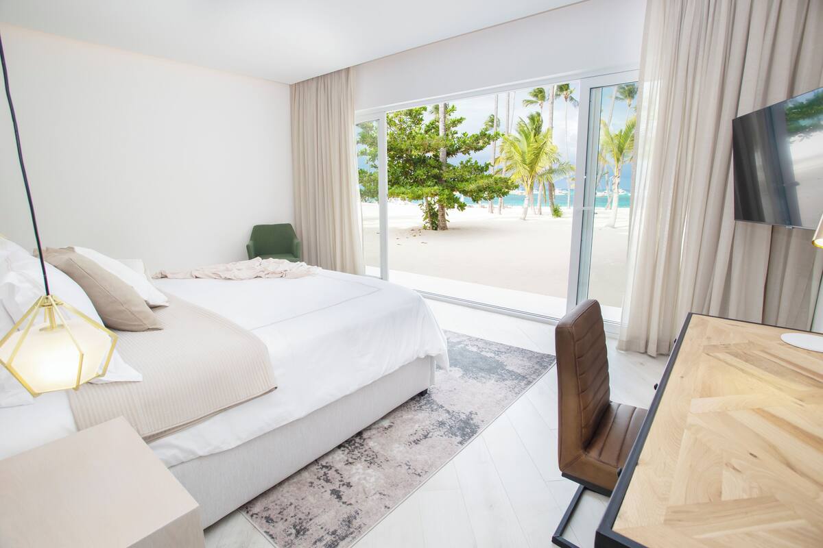 Une chambre d’hôtel avec un lit, un bureau, une chaise, une télévision et une vue sur la plage.