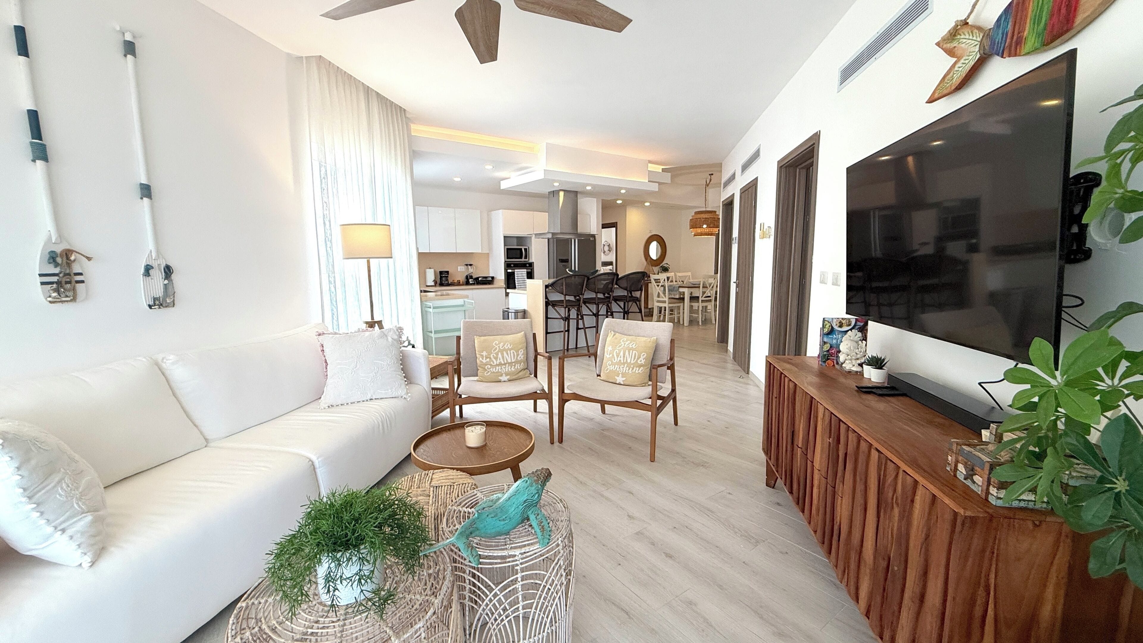 Una sala de estar moderna con un sofá blanco, dos sillones, una mesita de centro y un televisor sobre un mueble de madera.