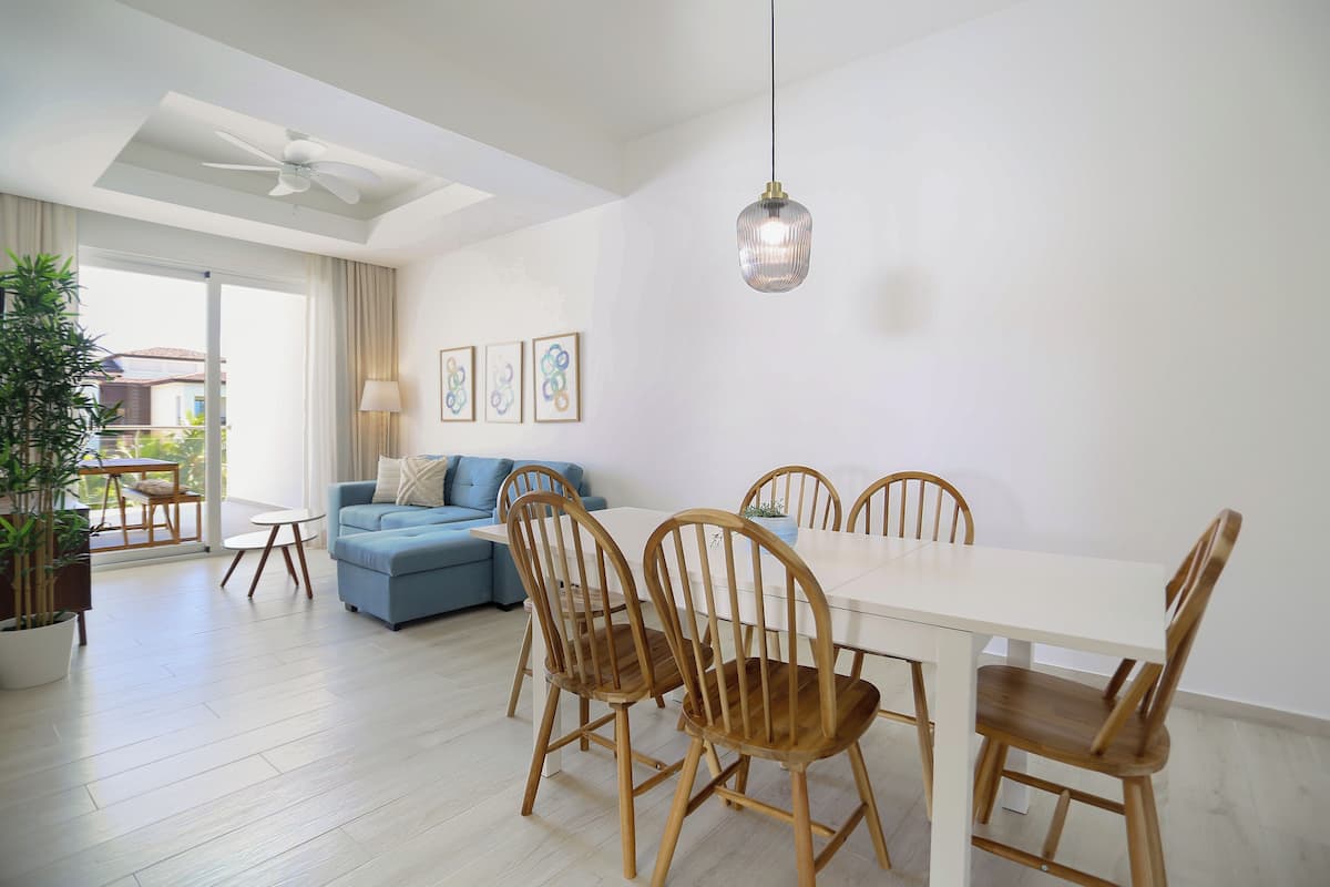 Un espace de salle à manger moderne avec une table blanche et des chaises en bois, un ventilateur de plafond et un luminaire suspendu.