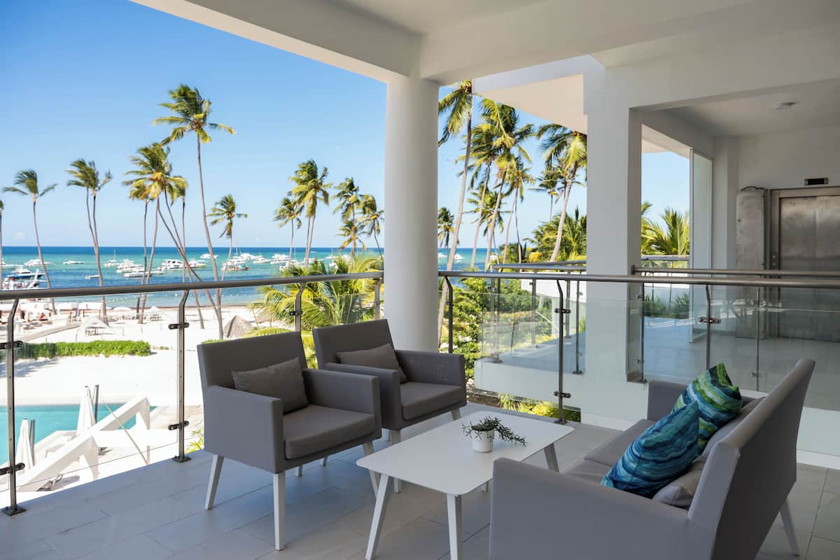 Un balcon avec vue sur la plage et l’océan, aménagé avec des chaises et une table.