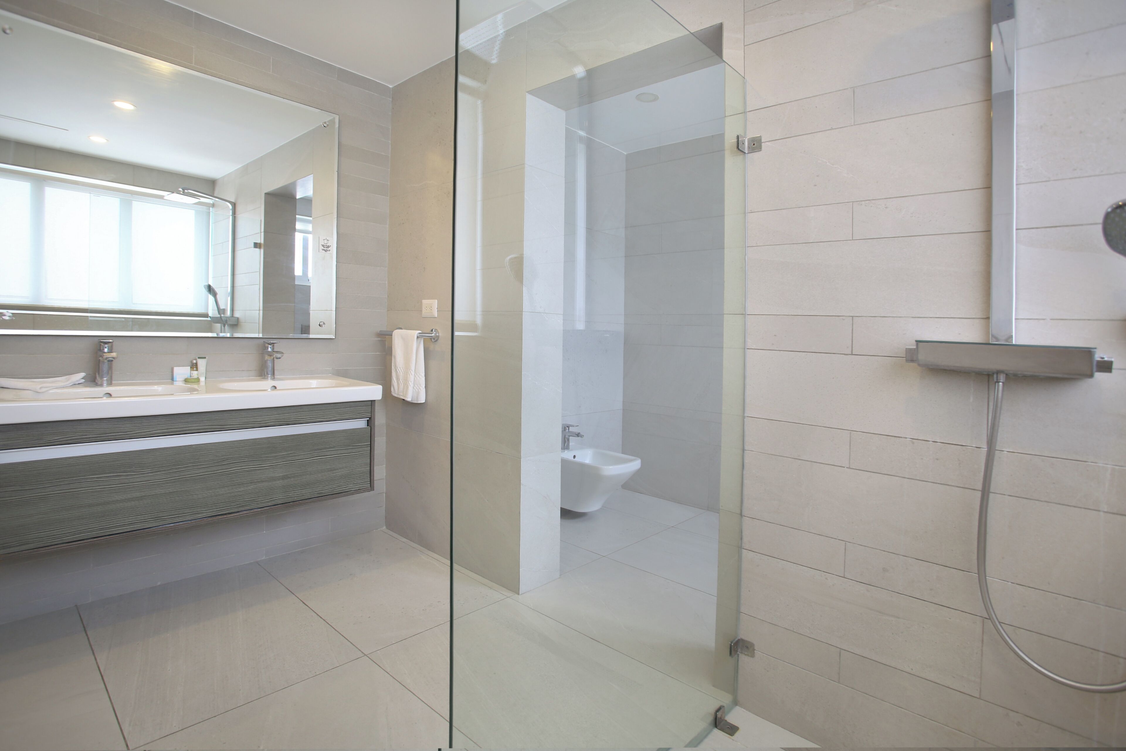 Un baño moderno con cabina de ducha de vidrio, un espejo grande y un tocador con lavabo y perchero para toallas.