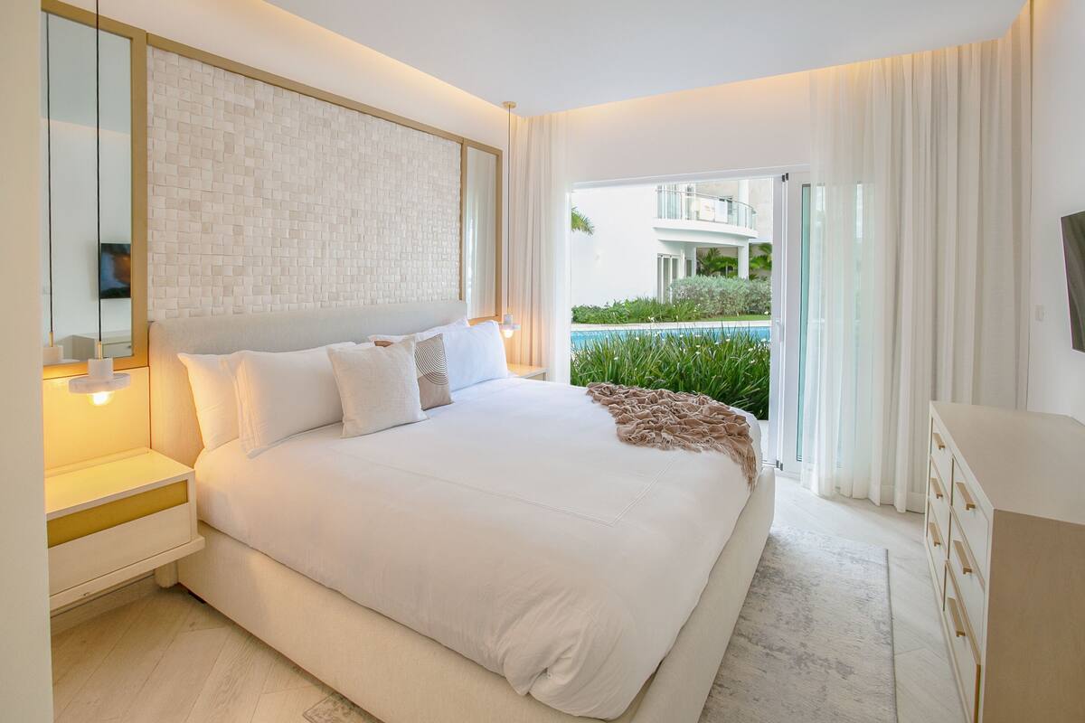 Une chambre moderne avec un grand lit, une table de chevet, une commode et une vue sur une piscine.
