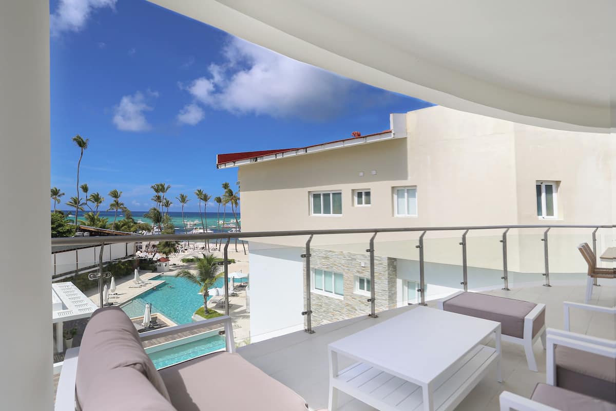 Un balcon donnant sur la piscine, des meubles blancs et un ciel d’un bleu éclatant.