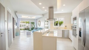 Une cuisine moderne avec des meubles blancs, un îlot central et un réfrigérateur en acier inoxydable.