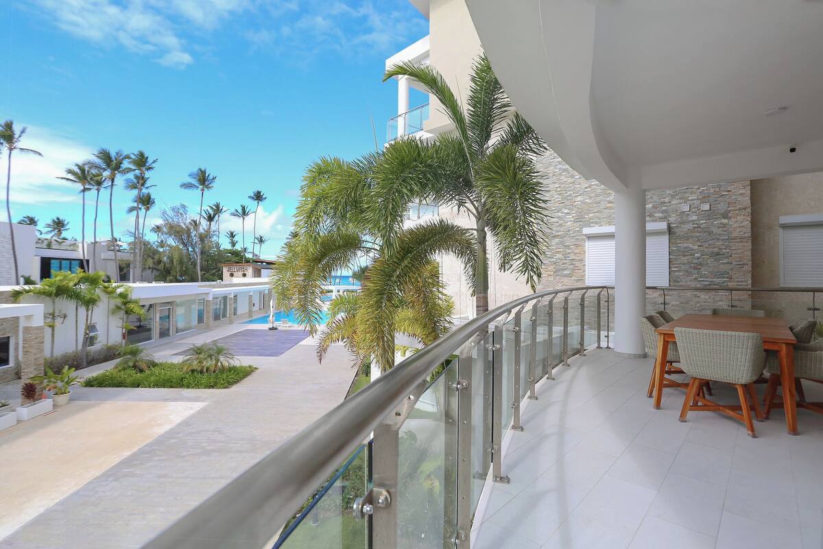 Un balcon donnant sur une piscine, des palmiers et un bâtiment portant l’inscription « JELLY WASH ».