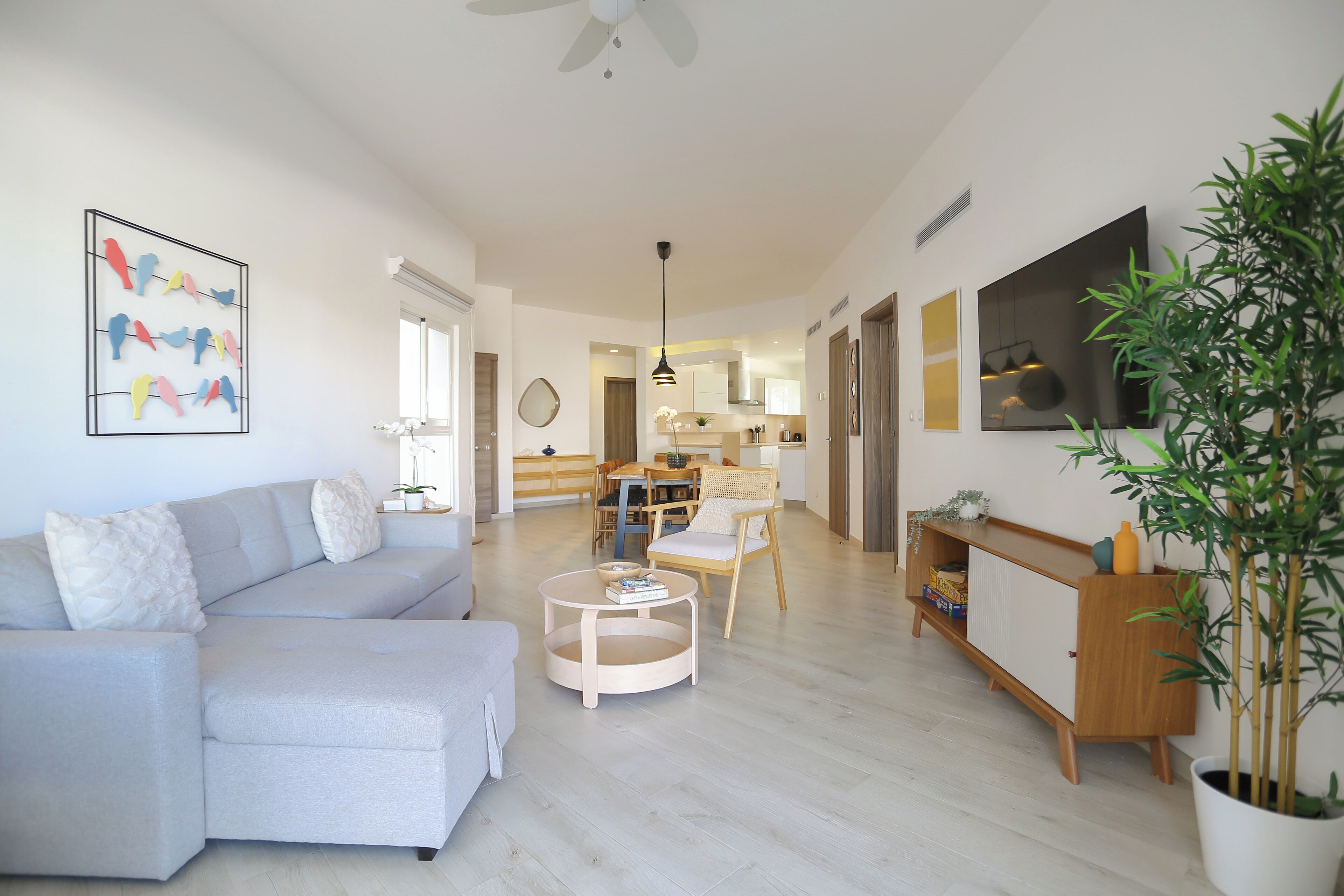 Una sala de estar moderna con un sofá seccional gris, una mesa redonda y un comedor con una mesa y sillas de madera.