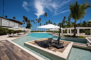 Un área de piscina con sillas de descanso y sombrillas, rodeada de palmeras y cielos despejados.