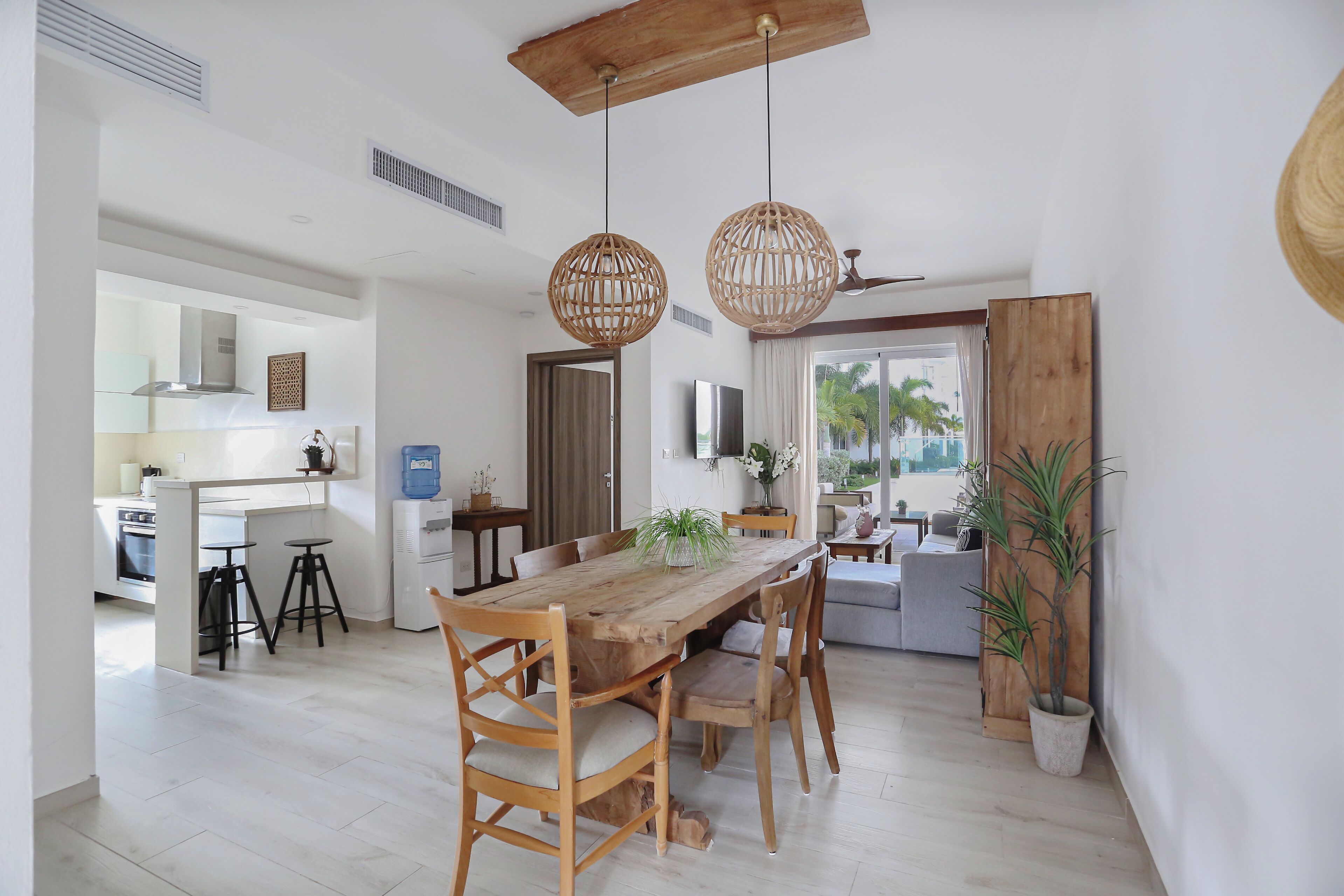 A spacious dining area with a wooden table and chairs, a kitchen in the background, and a view of the outdoors.