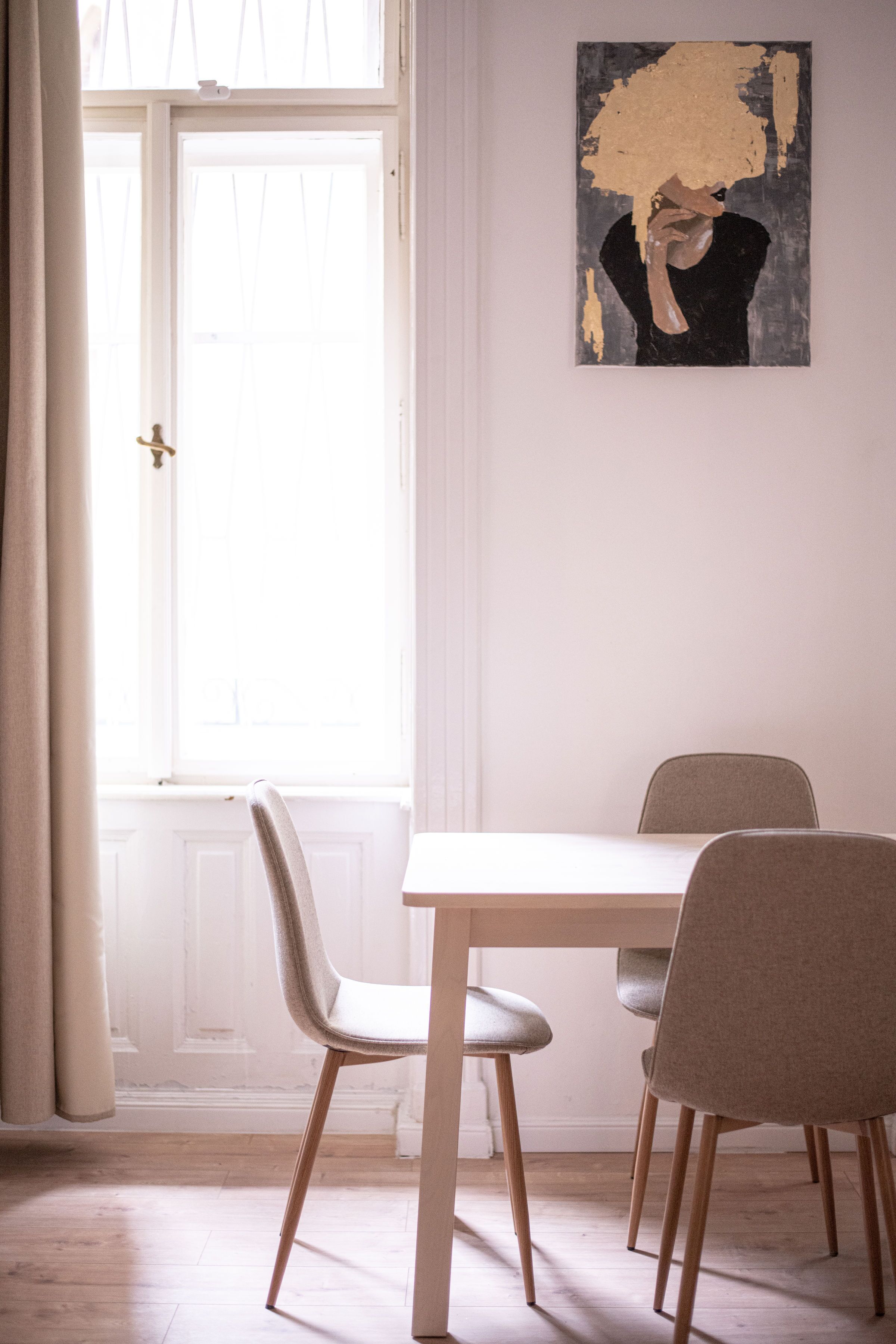 Un área de comedor con una mesa y sillas, una ventana con cortinas y un cuadro en la pared.