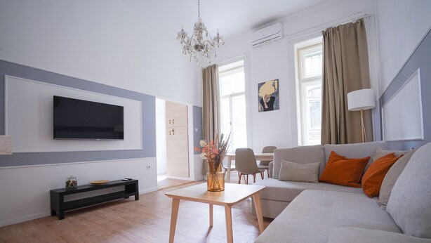A modern living room with a flat-screen TV, a sofa, a coffee table, and a chandelier. - Venus Apartments - Klauzál Apartment (Budapest)