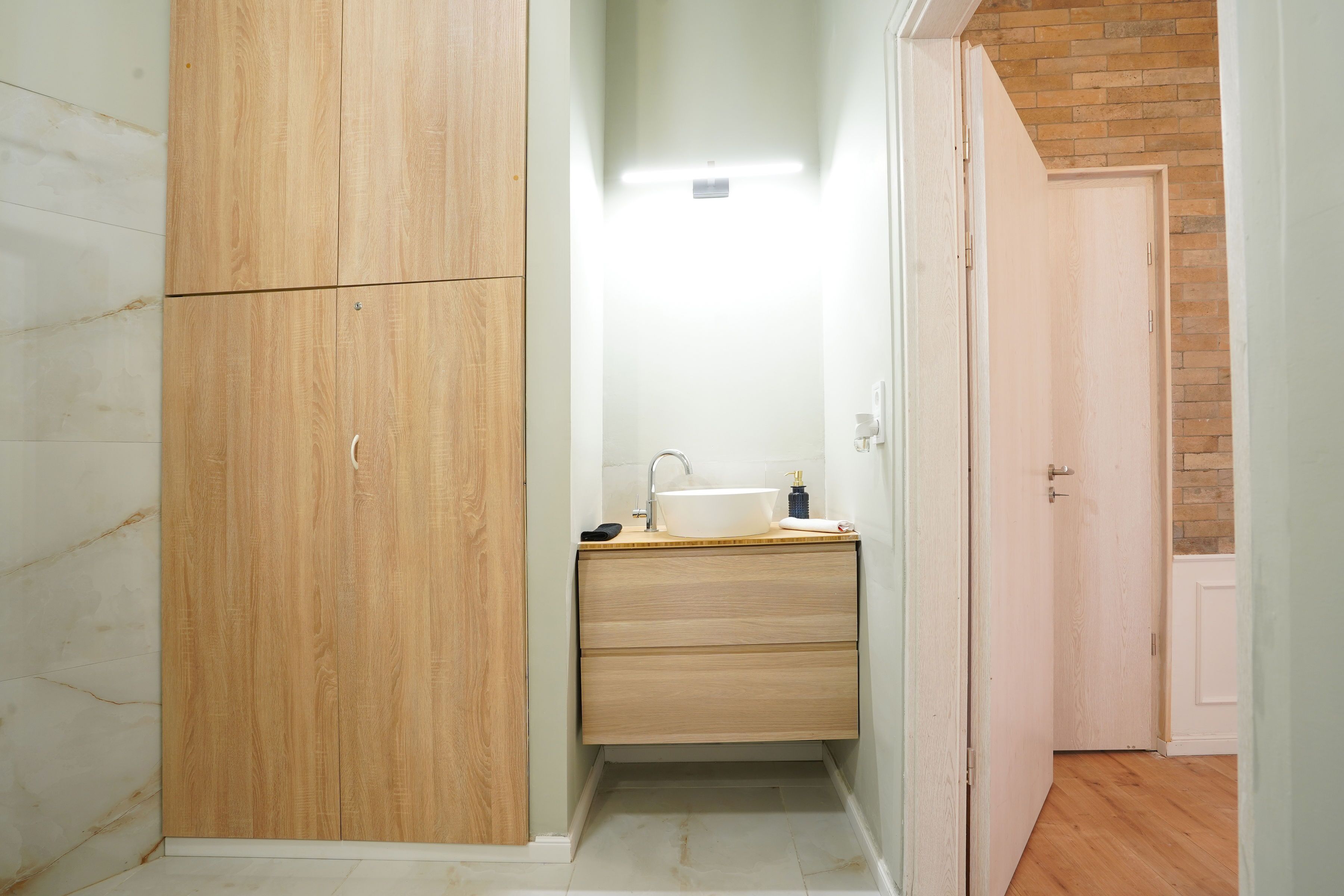 A small bathroom with a wooden wardrobe, a sink, and a mirror.