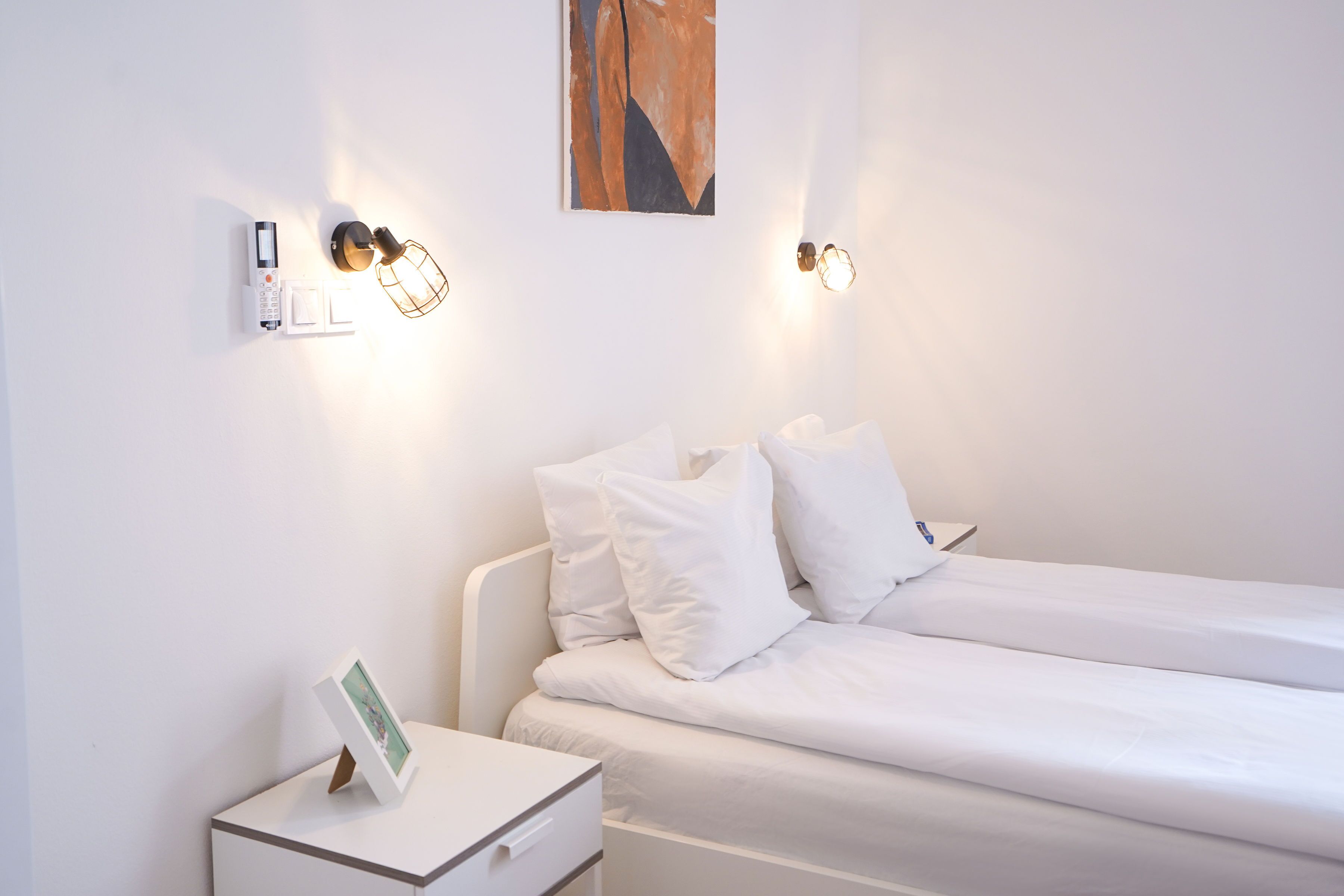 A minimalist hotel room with a bed, bedside table, and wall-mounted light fixtures.