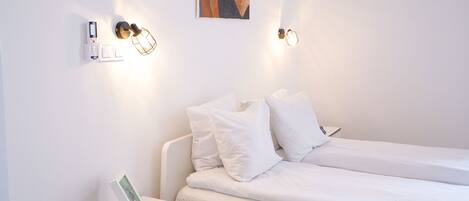 A minimalist hotel room with a bed, bedside table, and wall-mounted light fixtures.