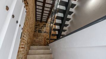 Eine Treppe mit einer Steinmauer an einer Seite und einer weißen Wand an der anderen, die zu einer Holzzieldecke mit einer Leuchte führt.