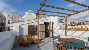 Un patio en la azotea con una pérgola de madera, una mesa de madera con sillas y un banco de madera.