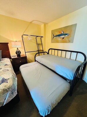 Un dormitorio con cama, mesita de noche, lámpara y un cuadro en la pared.