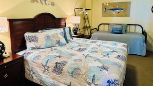 Une chambre à coucher avec un lit, une table de chevet, une lampe, un ventilateur de plafond et un tableau accroché au mur.