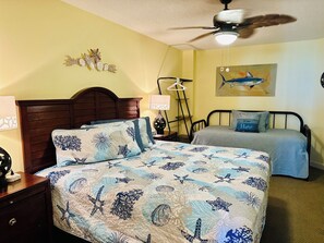 A bedroom with a bed, a nightstand, a lamp, a ceiling fan, and a painting on the wall.