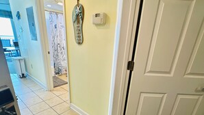 Un couloir avec un sol carrelé, une porte et un thermostat fixé au mur.