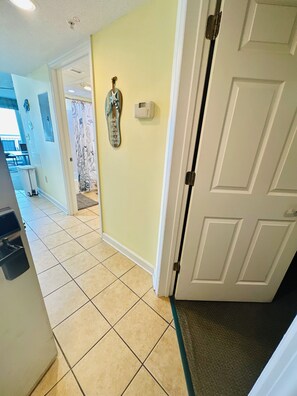 A hallway with a tiled floor, a door, and a wall-mounted thermostat.
