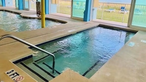 Une piscine intérieure à l’eau claire, dotée d’un plongeoir et offrant une vue sur l’extérieur.